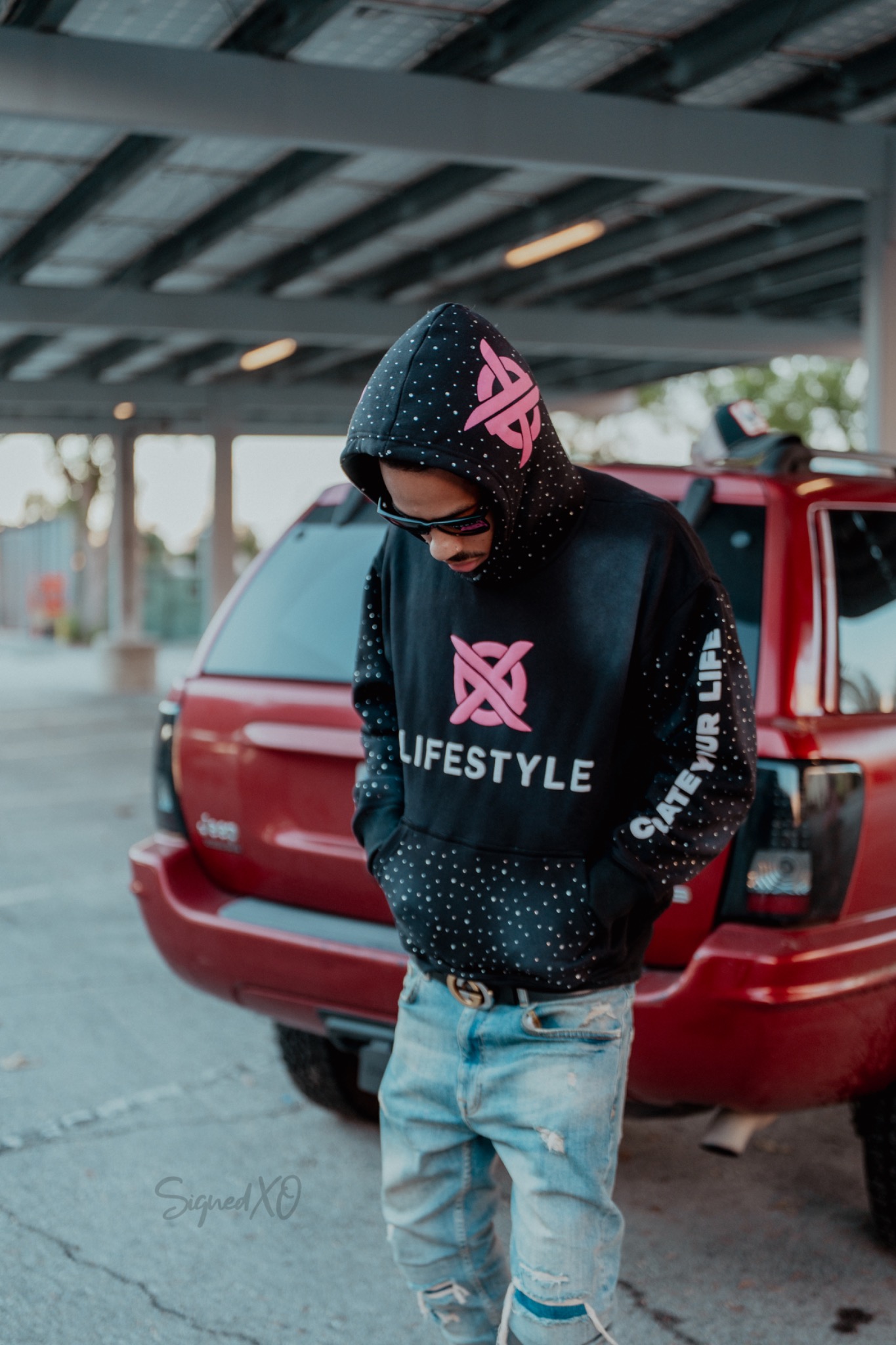 XO Lifestyle black hoodie with magenta logo worn outdoors